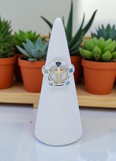 Ring with a cross design on a white cone stand with plants in the background